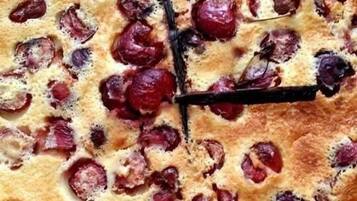 Una tarta redonda de color marrón dorado con trozos de fruta visibles en la parte superior, sobre un mantel a cuadros.