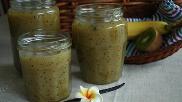 Three glass jars with a greenish mixture, a banana, kiwi, and a vanilla pod on a cloth.