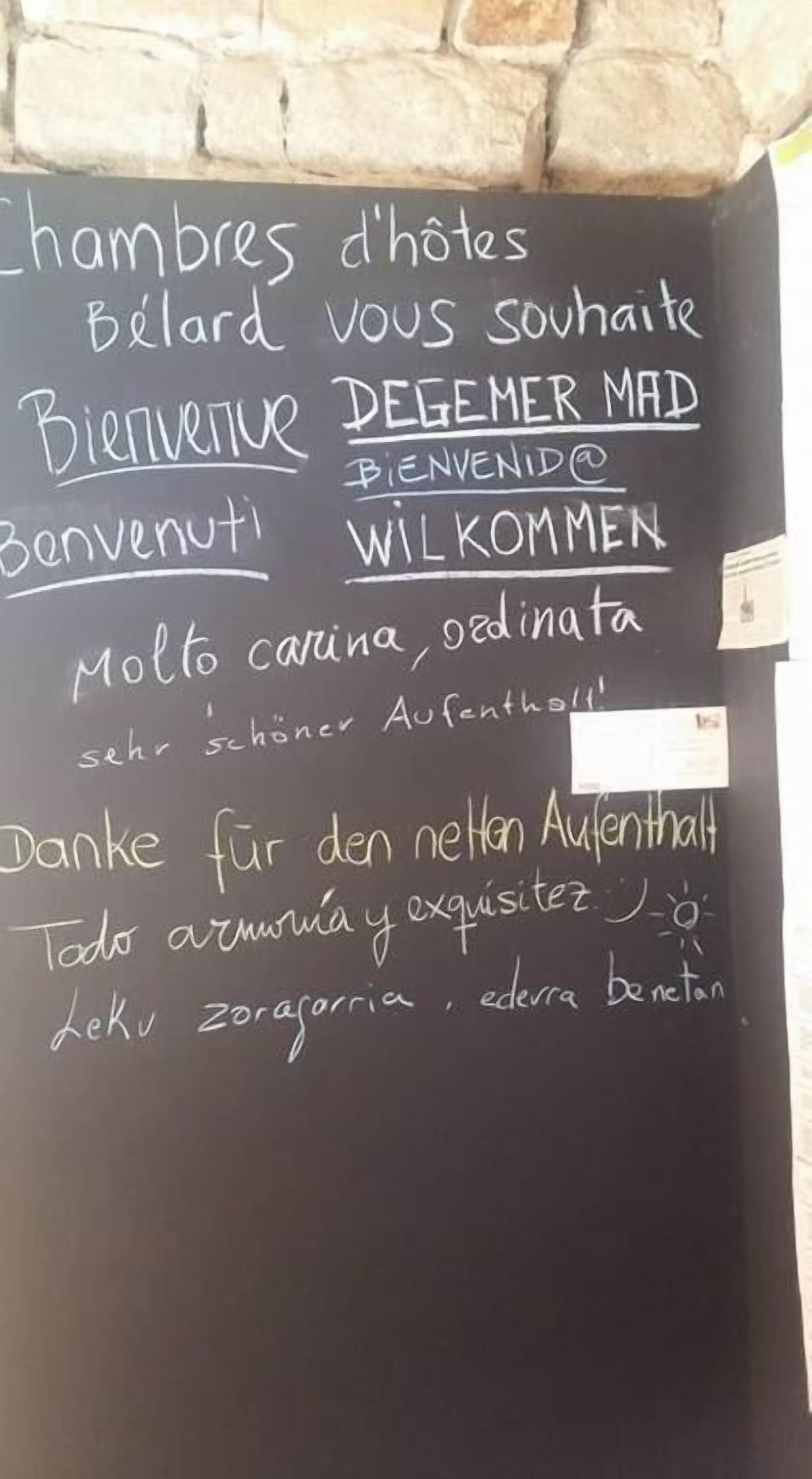 A blackboard with handwritten text in multiple languages, including English, French, and German, welcoming guests and expressing gratitude.
