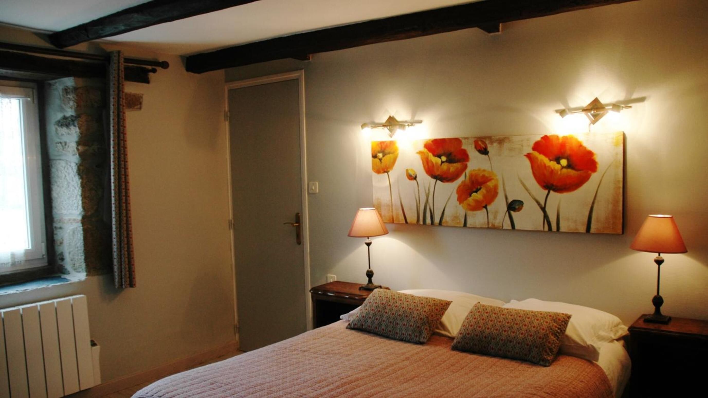 Un dormitorio con una cama, dos lámparas de noche, un radiador y un cuadro de flores en la pared.