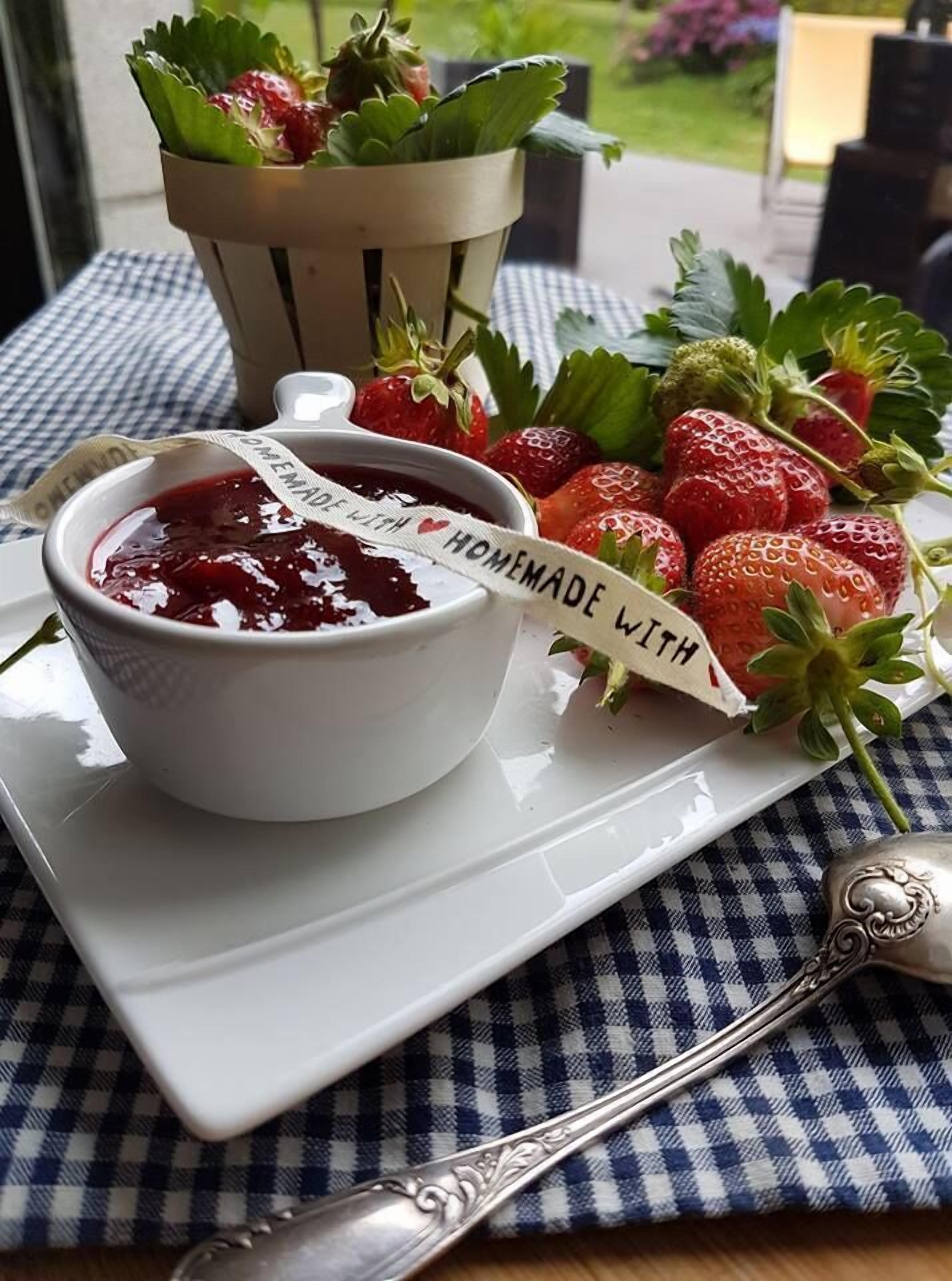 Un plateau avec des fraises et de la confiture maison, posé sur une nappe à carreaux.
