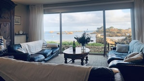 Un salón acogedor con un amplio ventanal que ofrece una vista panorámica del mar y la costa rocosa.