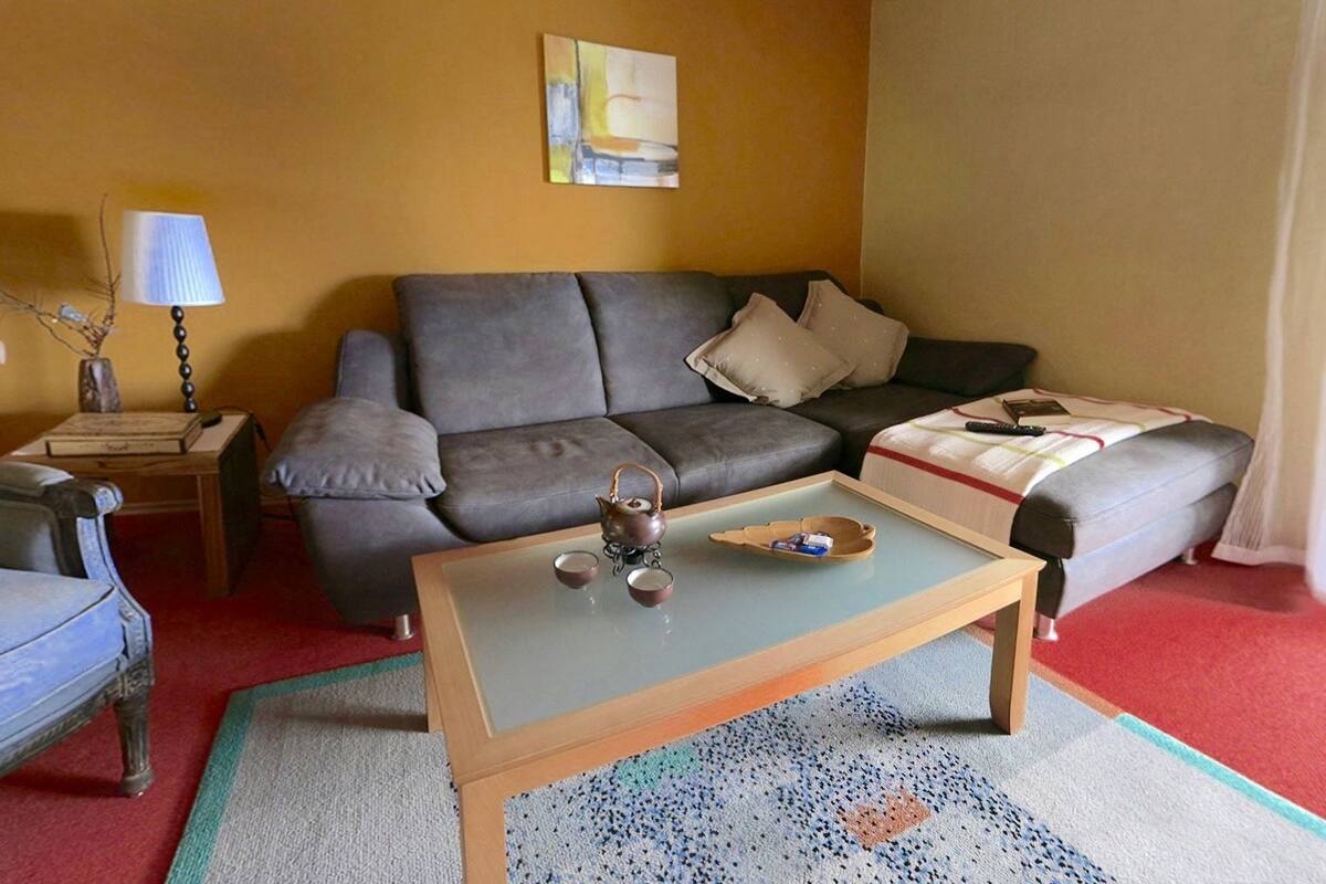 A living room with a grey sofa, a small wooden coffee table, a lamp, and a painting on the wall.