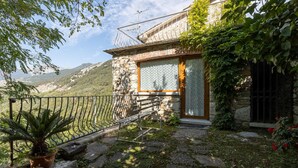 Una casa de piedra con puerta y ventana de madera, rodeada de follaje y un camino de piedra.