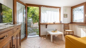 Una habitación con un armario de madera, una mesa con mantel de encaje, una silla y una ventana con cortinas de encaje.