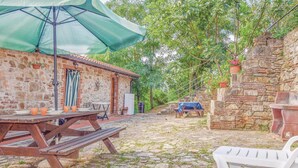 A rustic outdoor dining area with a stone wall, wooden table, and a green umbrella.