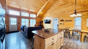 Interior acogedor de una cabaña con techo de madera, una isla central con armarios, un sofá y un comedor con sillas.