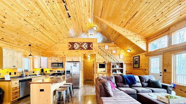 Amplio interior de cabaña con detalles de madera, una cocina, una sala de estar con un sofá seccional grande y un comedor con mesa y sillas de madera.
