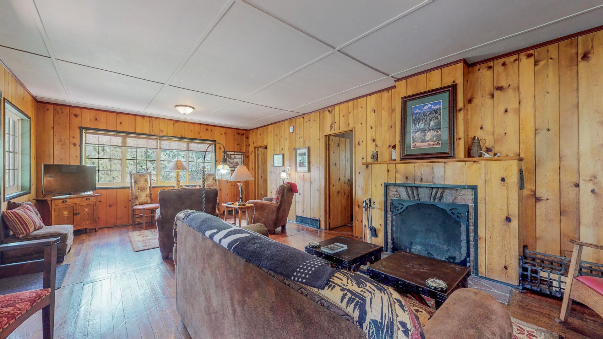 A cozy cabin interior with a fireplace, wooden walls, a sofa, a television, and a dining table.