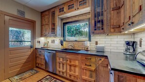 Una cocina con armarios de madera, lavavajillas empotrado, ventana con vistas a árboles y cafetera.