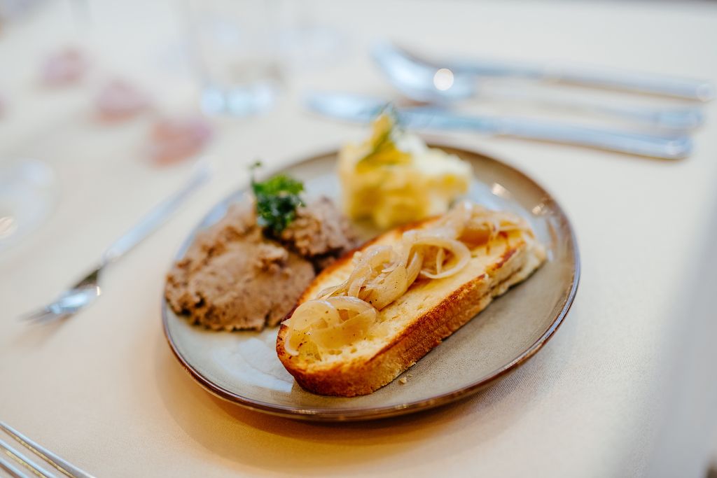 A plate with a slice of bread topped with onions, a dollop of mustard, and a small portion of meat.