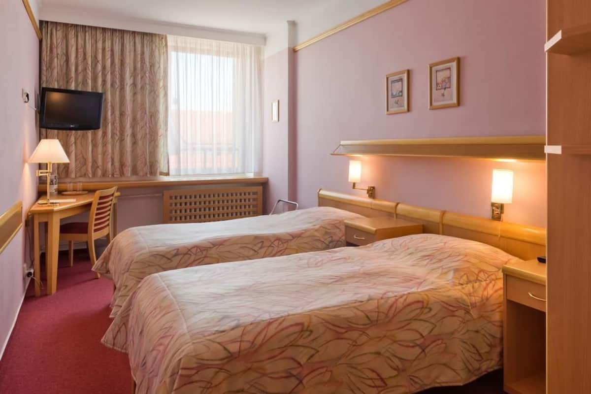 A hotel room with two beds, a desk, a chair, a TV, and a window with curtains.