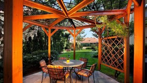 A covered patio with a round table and chairs, surrounded by a wooden pergola structure.