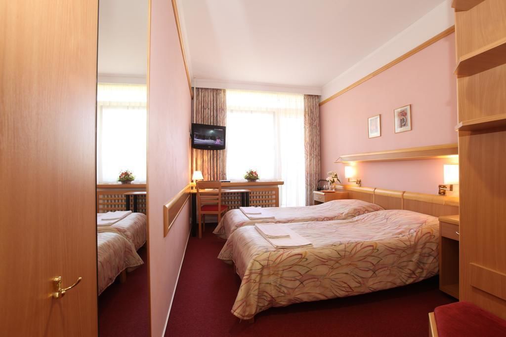 Quarto de hotel com duas camas, uma escrivaninha, televisão e uma janela com cortinas.