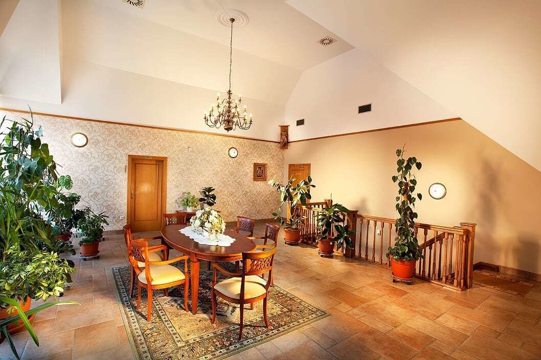 A dining area with a wooden table, chairs, and a chandelier. There are potted plants around the room.