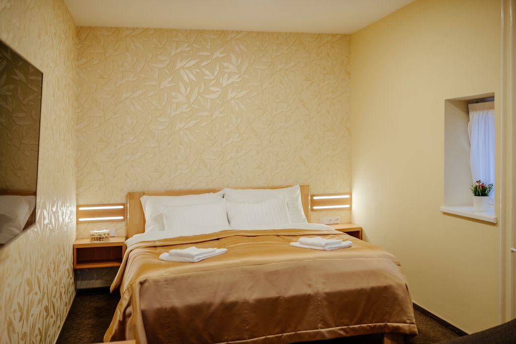 A hotel room with a bed, nightstands, a window with a curtain, and a wall with a leaf pattern.