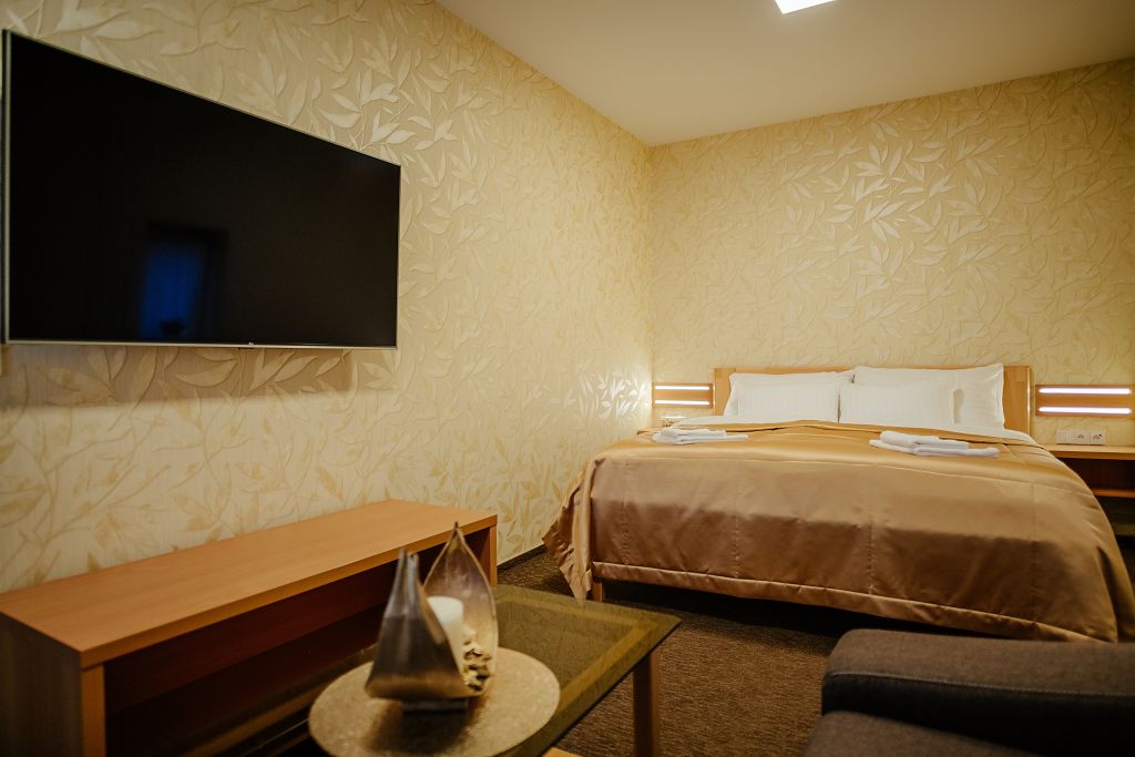 Ein Hotelzimmer mit Bett, Wandfernseher, Nachttisch und einer kleinen Sitzecke.