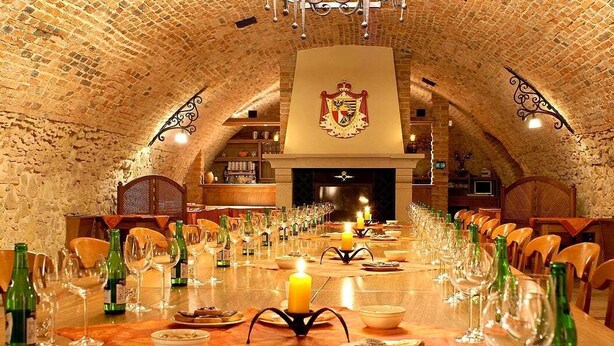 A long dining table set for a meal in a room with a vaulted brick ceiling and a coat of arms above the fireplace.