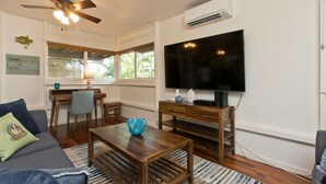 Una sala de estar con ventilador de techo, un televisor de pantalla plana, una mesa de centro de madera, un sofá y un escritorio con una silla.