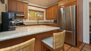 Una cocina con armarios de madera, un refrigerador de acero inoxidable, una cafetera y dos sillas de mimbre.