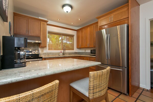 A kitchen with wooden cabinets, a stainless steel refrigerator, a coffee maker, and two wicker chairs.