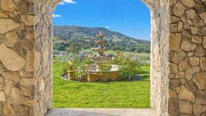Un arc en pierre encadre une fontaine à plusieurs niveaux, le tout étant entouré d’une pelouse bien entretenue et ayant pour toile de fond un paysage montagneux.