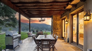 Une terrasse extérieure avec une table et des chaises en bois, un barbecue et un mur en pierre.