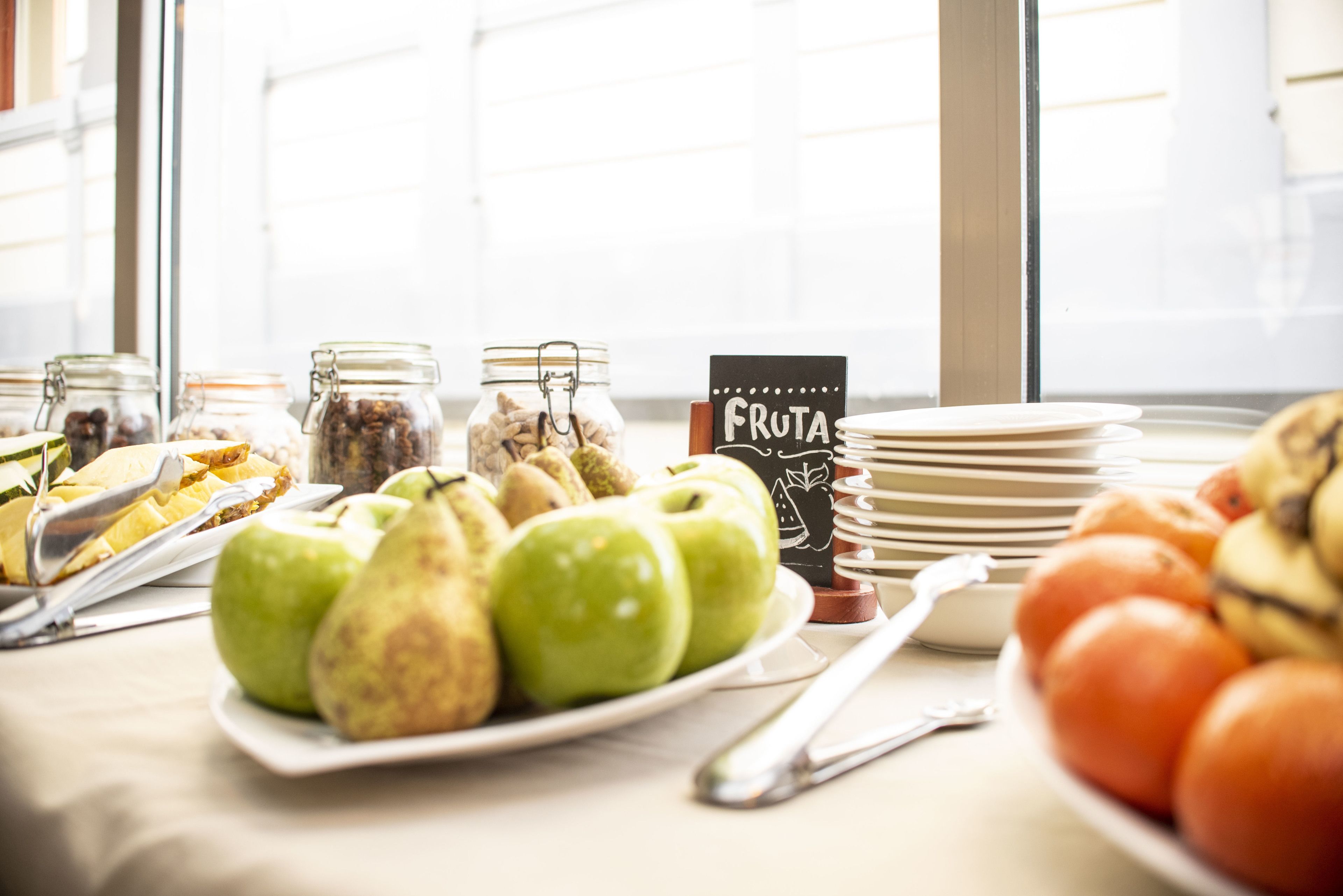 A breakfast buffet with various fruits, including apples and oranges, and a sign labeled "FRUTA".