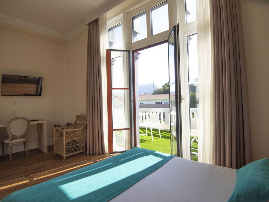 A hotel room with a bed, a desk, a chair, and a balcony with a view of the outdoors.
