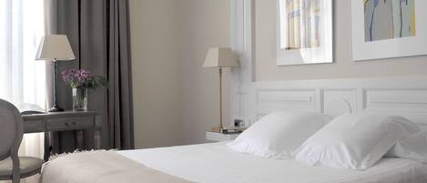 A neatly made bed with white linens, a bedside table with a lamp, and a chair.