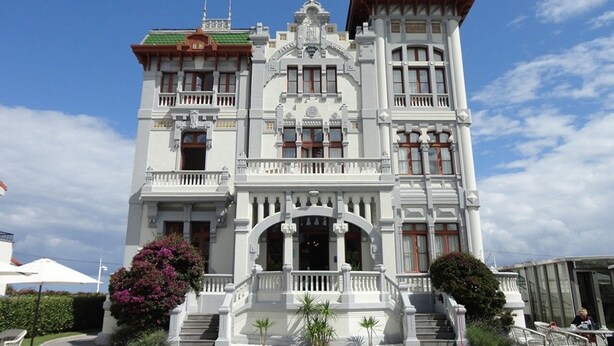 Un imposant bâtiment blanc, doté de nombreux balcons et d’une entrée centrale.