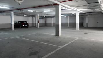 An empty parking garage with concrete pillars, white walls, and fluorescent lighting.