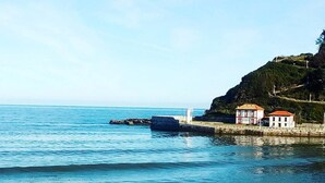 Un paysage côtier offrant une vue dégagée sur la mer, avec une côte rocheuse et un petit bâtiment doté d’un toit rouge.