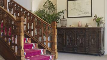 A wooden staircase with pink carpeted steps, a dark wooden cabinet with decorative carvings, and a framed artwork on the wall.