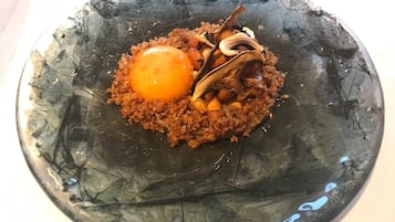 Una losa de vidrio oscura con una yema de huevo central, migas crujientes y setas deshidratadas.