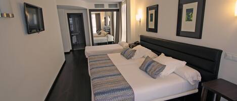 A hotel room with two beds, a dark wooden floor, and a mirror on the wall.