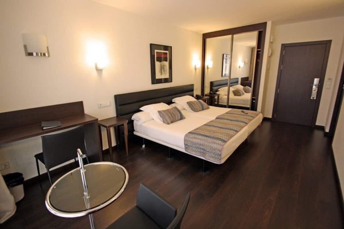 Een hotelkamer met een bed, een bureau, een stoel, een ronde tafel en een spiegel.