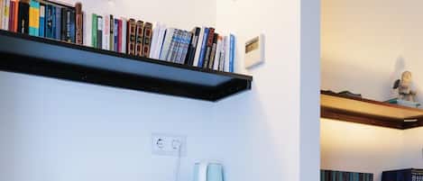 A compact living space with a red retro-style cabinet, a bookshelf filled with books, a small table with a cup and saucer, and a wall-mounted light fixture.