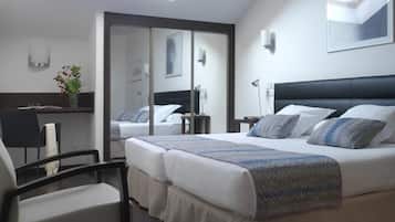 Hotelkamer met een groot bed, een bureau en een stoel. Er is een spiegel aan een wand en een dakraam boven het bed.
