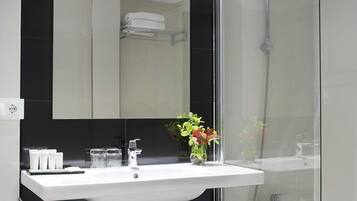 A modern bathroom with a white sink, a glass shower enclosure, and a large mirror above the sink.