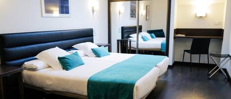 A modern hotel room with a large bed, a desk, and a mirror.