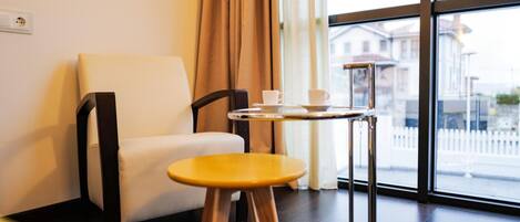 Una habitación moderna con una silla blanca, un taburete de madera y una mesa con taza y plato.