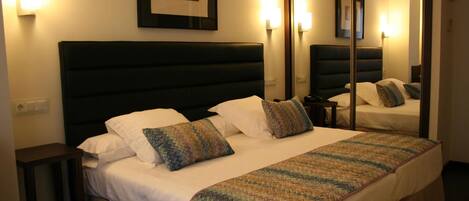 A hotel room with a large bed, a bedside table, a mirror, and wall-mounted lights.