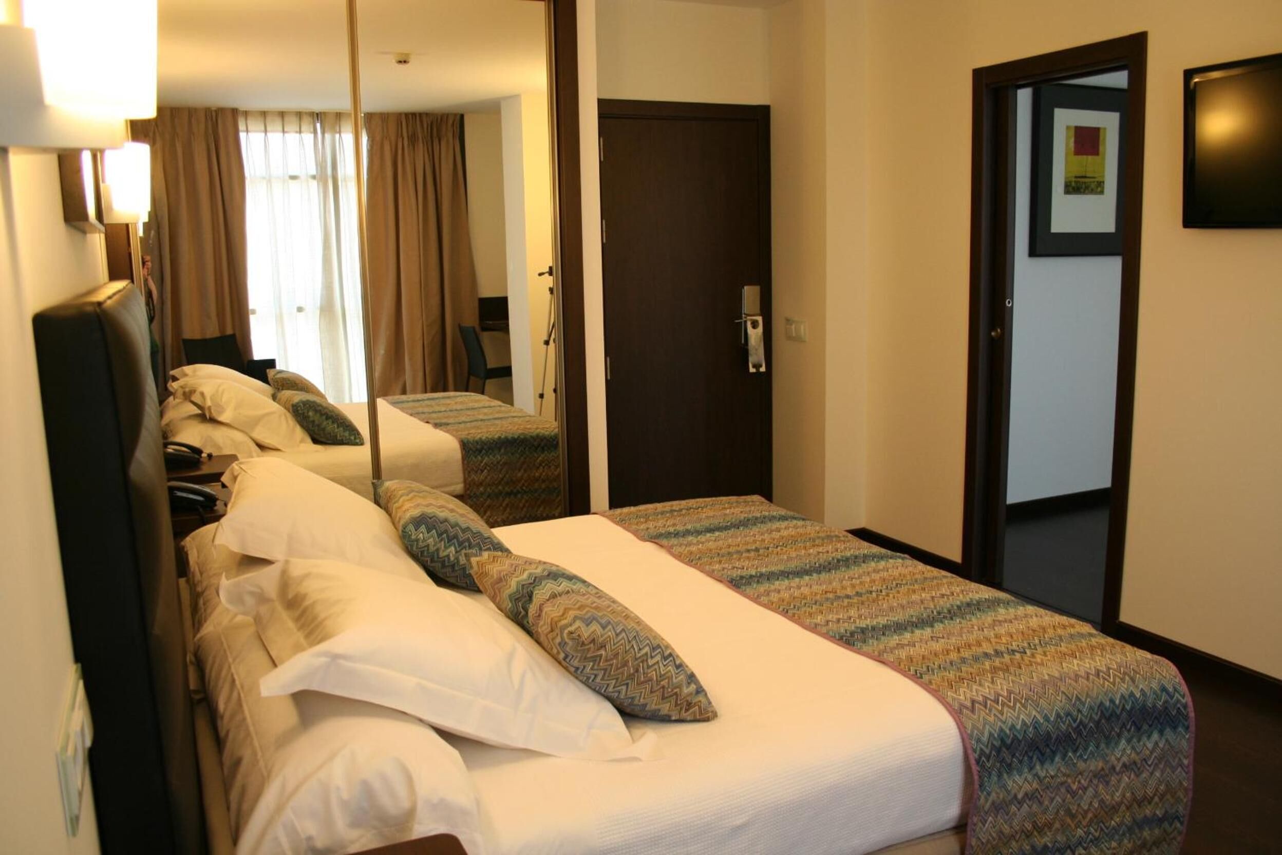 Habitación de hotel con dos camas, un espejo, una puerta y un cuadro en la pared.