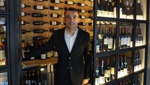 Un hombre con traje frente a una pared de botellas de vino.