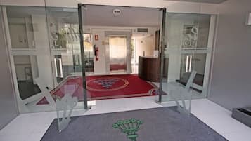 A hotel lobby with a red carpet, glass doors, and a reception desk.