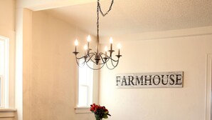 Een eetruimte met een grote tafel, banken, een kroonluchter en een 'FARMHOUSE' bord op de muur.