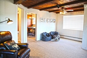 Relax in this inviting living room with a leather armchair, bean bag chair, and ottoman, surrounded by framed artwork and a large window.