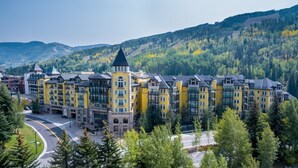 A multi-story hotel with a central tower, surrounded by lush greenery and mountains in the background.