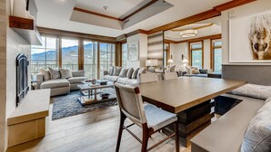 A spacious living room with a large wooden dining table, multiple seating areas, and large windows offering a mountain view.